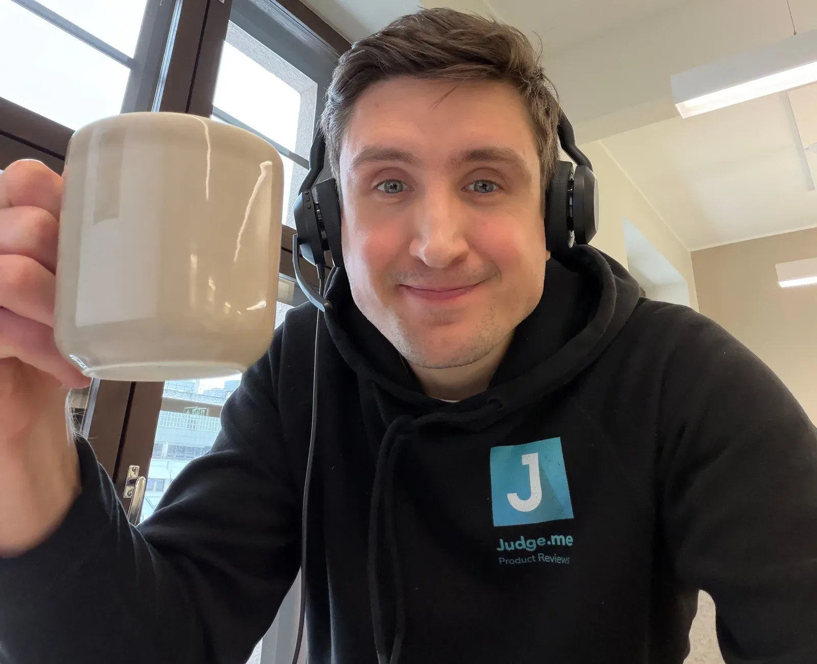 Karri in a Judge.me hoodie, raising a mug to the camera