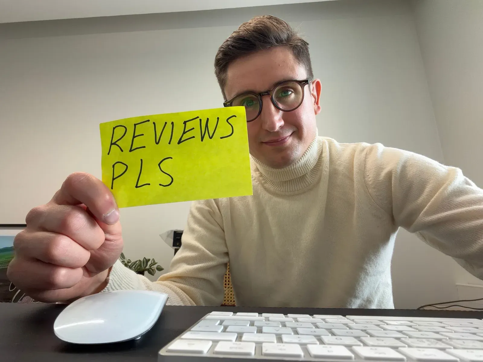 Karri at his desk holding up a sticky note that reads “Reviews pls”