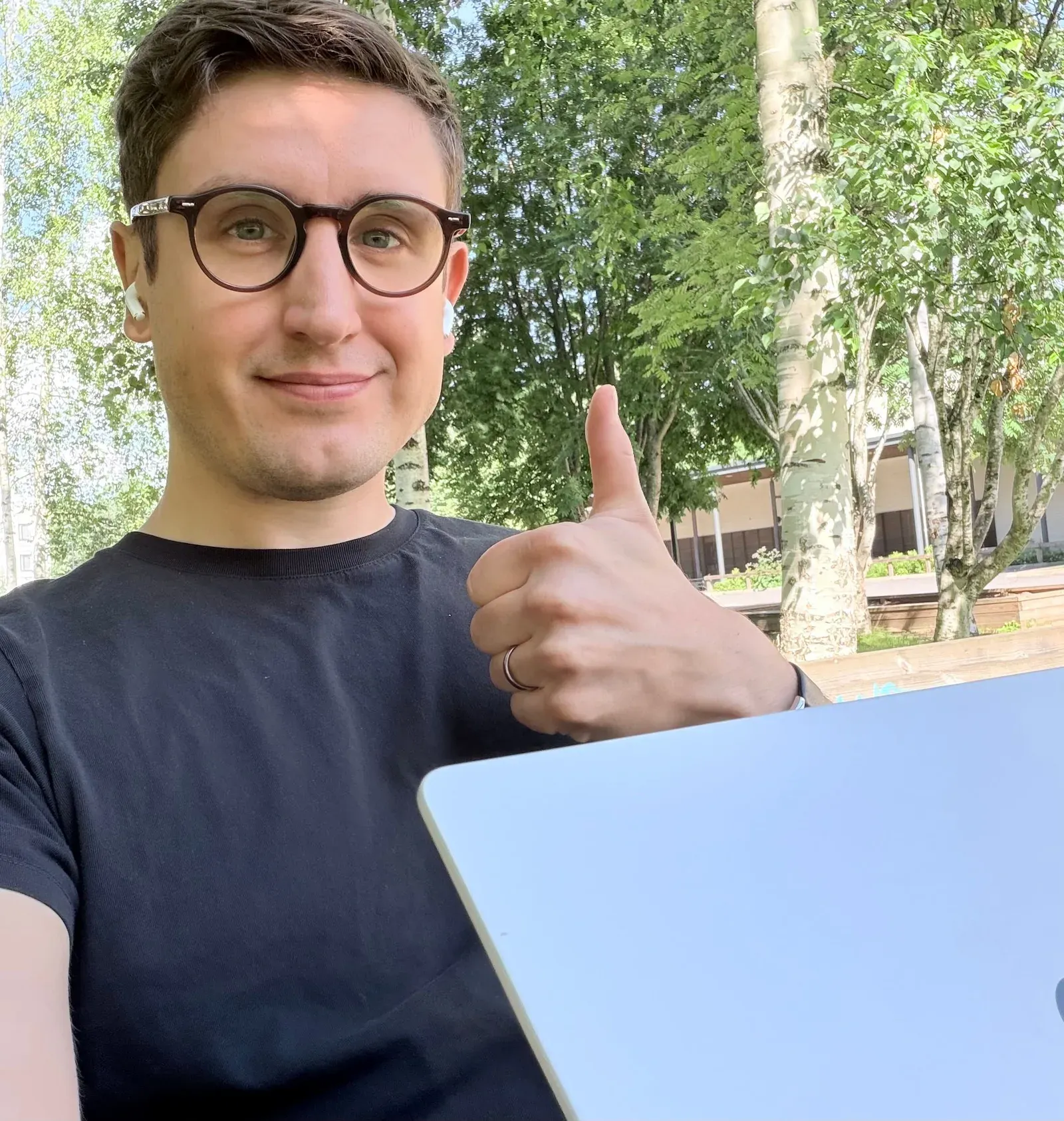 Karri outdoors with his laptop, giving a thumbs up
