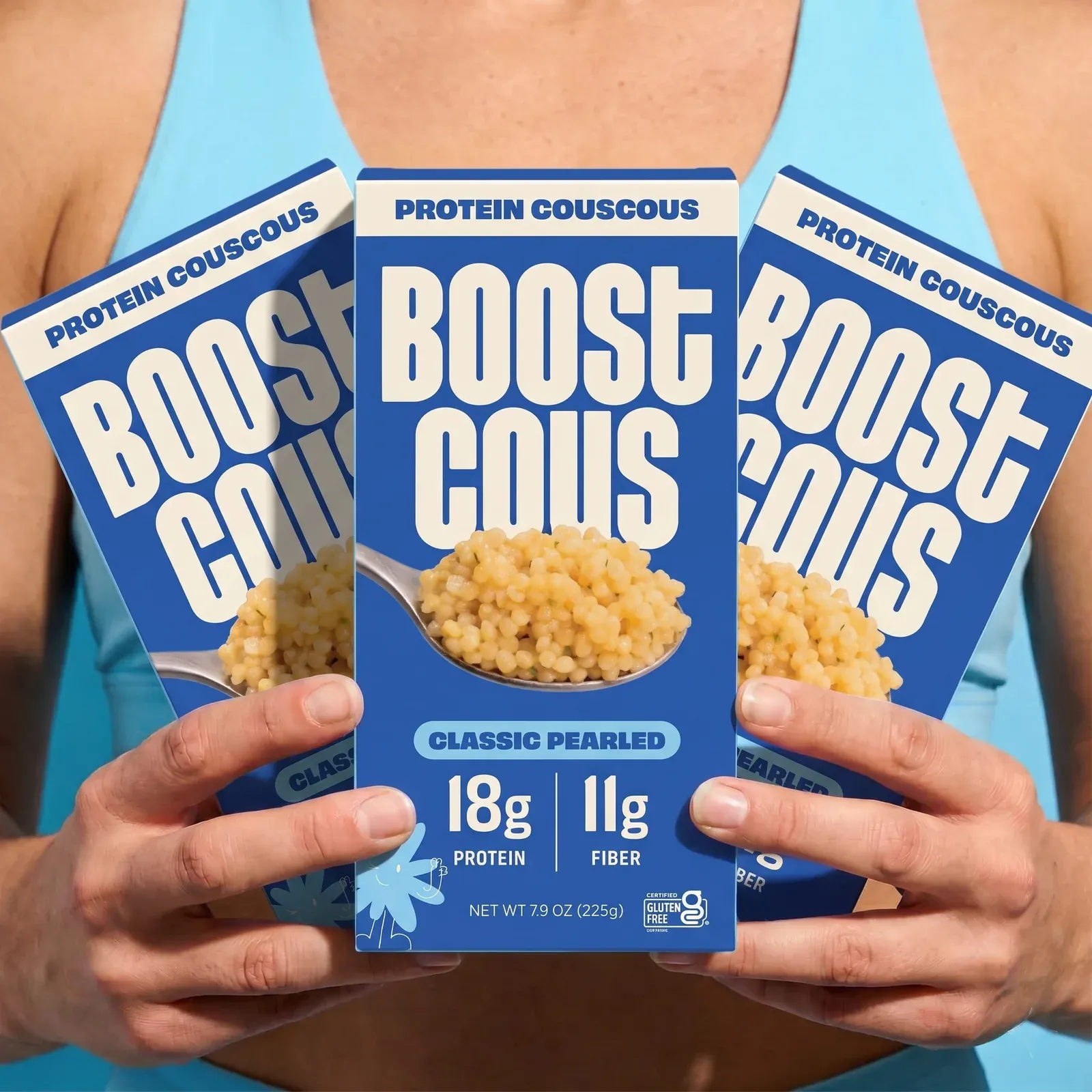 Hands holding up three boxes of Boostcous Classic Pearled protein couscous